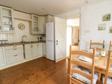 A kitchen with white cabinets a wooden dining table with chairs and a refrigerator at Spring Cottage in Pentre-Cwrt