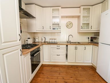 A kitchen with white cabinets wooden countertops appliances and a wooden floor at Spring Cottage in Pentre-Cwrt