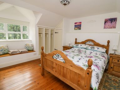 A bedroom with a wooden bed and side tables near a window seat with cushions and shelves at Spring Cottage in Pentre-Cwrt