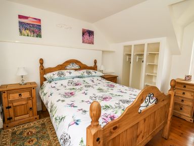 A bedroom with a wooden bed and floral bedding with wooden bedside tables and built in wardrobes at Spring Cottage in Pentre Cwrt