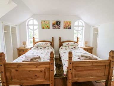 A bedroom with two wooden single beds and bedside tables under arched windows at Spring Cottage in Pentre-Cwrt