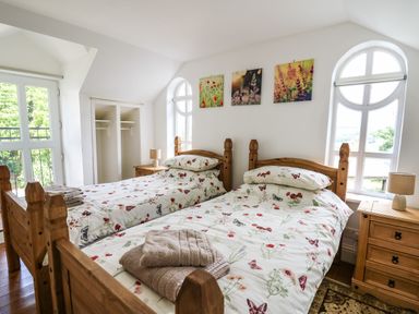 A bedroom with two wooden single beds with floral bedding two bedside tables with lamps and floral pictures on the wall at Spring Cottage in Pentre Cwrt