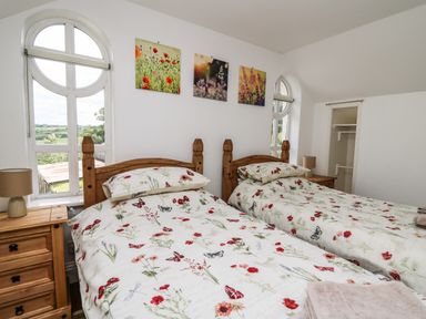 A bedroom with two single beds floral bedding wooden bedside tables with lamps and three floral pictures on the wall at Spring Cottage in Pentre-Cwrt