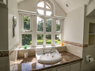 A bathroom sink under a large window with two toy animals on the windowsill at Spring Cottage in Pentre-Cwrt
