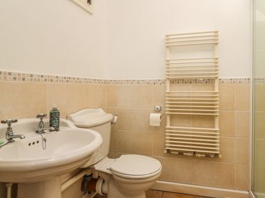 A bathroom with a sink a toilet a wall-mounted towel radiator and tiled walls at Spring Cottage in Pentre-Cwrt