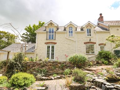 A garden with plants and rocks in front of a stone house with white walls and multiple windows at Spring Cottage in Pentre-Cwrt
