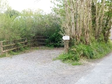 A gravel driveway leading to a wooded area with trees and a wooden fence with a Spring Cottage sign on a tree at Pentre-Cwrt