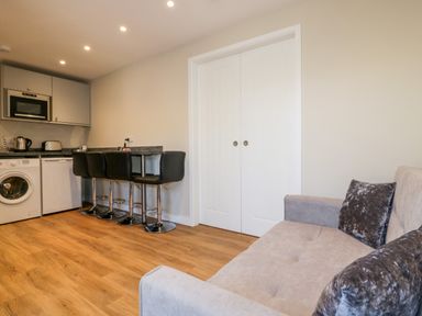 A small kitchen area with appliances and bar stools next to a sofa in a living space at The Granary in Helland near Bodmin