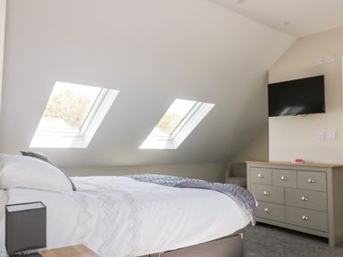A bedroom with two skylight windows a bed a gray dresser and a wall-mounted TV at The Granary in Helland near Bodmin
