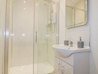 A bathroom with a glass shower enclosure a white sink with a faucet a soap dispenser and a mirror at The Granary in Helland near Bodmin
