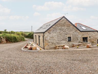 A stone building with a slate roof and picnic tables outside on a gravel area at The Granary in Helland near Bodmin