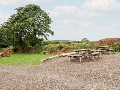 An outdoor area with wooden picnic tables on gravel near grass and trees at The Granary in Helland near Bodmin