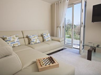A living room with a beige sectional sofa with patterned cushions a chessboard on the sofa glass side table and a wall-mounted television at Crowthers in Dartmouth