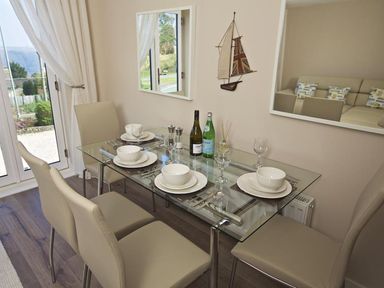 A dining area with a glass table set for four with beige chairs and a wall decoration of a sailboat at Crowthers in Dartmouth