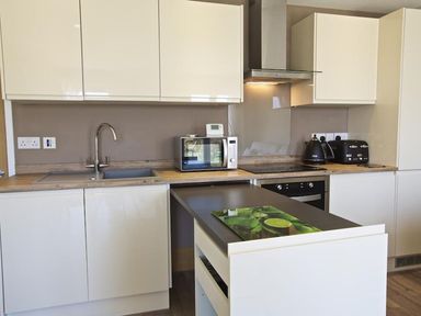 A kitchen with white cabinets a sink a microwave toaster kettle and an island at Crowthers in Dartmouth