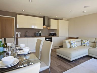 A kitchen with white cabinets a dining table with dishes and a beige sofa with patterned pillows at Crowthers in Dartmouth