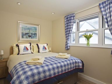 A bedroom with a bed with sailboat pillows a painting of sailboats and a window with blue plaid curtains and yellow flowers at Crowthers in Dartmouth