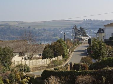 A sloped road lined with trees and fences with houses on either side and hills in the background at Crowthers in Dartmouth