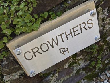 A metal sign with the word Crowthers mounted on a stone wall with plants around it at Crowthers in Dartmouth