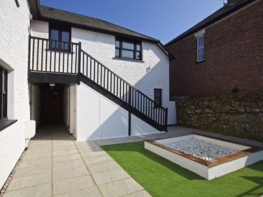 An outdoor patio area with stone tiles artificial grass a white pebble garden bed and a staircase leading to an upper door at Crowthers Dartmouth