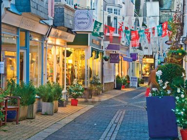 A street with shops decorated with hanging flags and holiday lights at Crowthers in Dartmouth