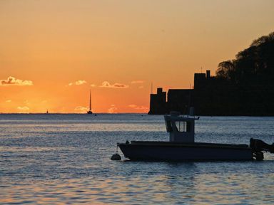 A boat on water at sunset with a castle and trees in the background at Crowthers in Dartmouth