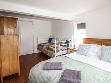 A bedroom with a double bed and a single bed a wooden wardrobe and a bedside table with a lamp at Seaside House in Weymouth