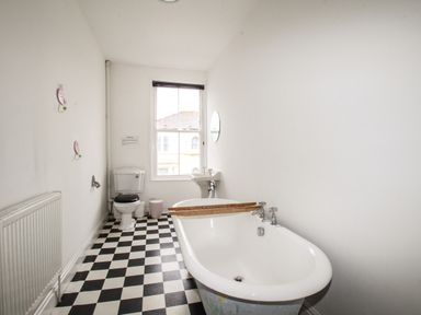 A bathroom with a black and white checkered floor a bathtub a toilet a sink and a window at Seaside House in Weymouth