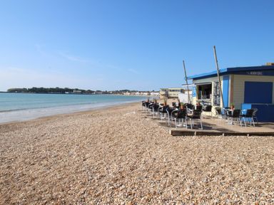 A pebble beach with tables and chairs outside a small beach cafe by the sea at Seaside House in Weymouth