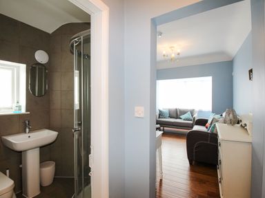 A bathroom with a shower and sink next to a living room with sofas and a dresser at Seaside House in Weymouth