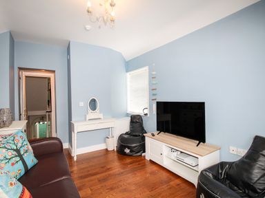 A living room with a television on a stand two black bean bags a white desk with a mirror and a brown sofa with cushions at Seaside House in Weymouth