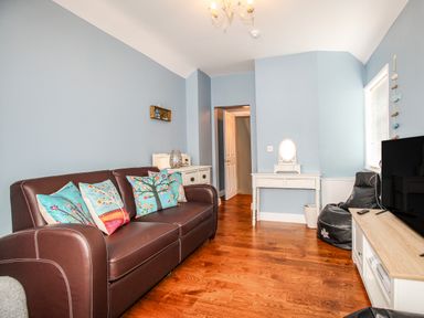 A living room with a brown sofa with colorful cushions a white dressing table a black bean bag a television on a wooden stand and blue walls at Seaside House in Weymouth
