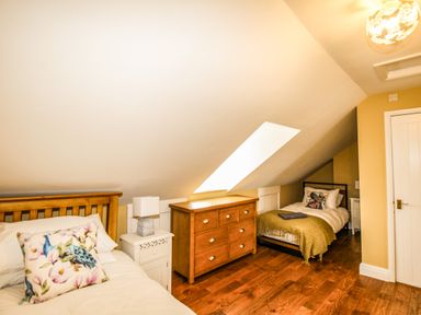 A bedroom with two single beds a wooden dresser and bedside tables under a sloped ceiling at Seaside House in Weymouth