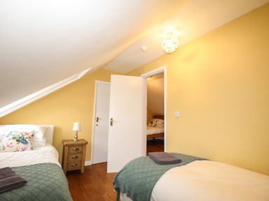 A bedroom with two single beds side table lamp open door showing another room with bed at Seaside House in Weymouth