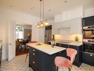 A kitchen with an island, pink chairs, tiled floor, and an adjacent dining room at Seaside House in Weymouth
