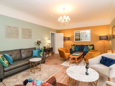 A living room with multiple sofas armchairs coffee tables lamps and wall art at Seaside House in Weymouth