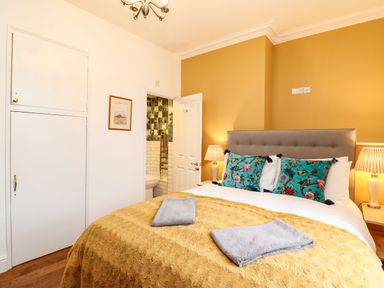 A bedroom with a bed with pillows and blankets bedside tables with lamps a door leading to a bathroom and a cabinet on the wall at Seaside House Weymouth