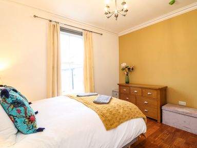 A bedroom with a bed that has blue pillows and a yellow blanket next to a wooden dresser with a vase of flowers at Seaside House in Weymouth