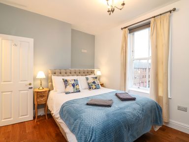 A bedroom with a double bed blue bedspread two bedside lamps and a window with cream curtains at Seaside House in Weymouth