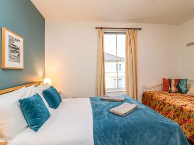 A bedroom with a double bed with blue pillows and blankets and a single bed with a floral blanket at Seaside House in Weymouth