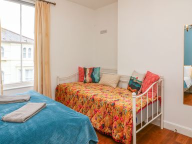 A bedroom with a bed covered with a blue blanket and towels and a daybed with colorful cushions and a floral bedspread at Seaside House in Weymouth