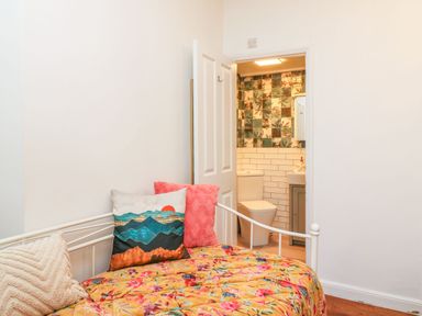 A room with a bed covered in a floral blanket and decorative pillows next to an open door leading to a bathroom with a toilet and floral and white tiled walls at Seaside House in Weymouth