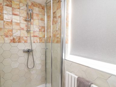 A shower area with hexagonal and square tiles and a glass shower door with a towel on a radiator at Seaside House in Weymouth