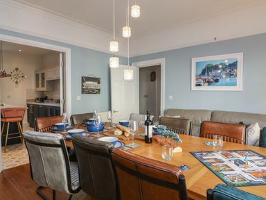 A dining room with a wooden table set for a meal and a board game with chairs around at Seaside House in Weymouth