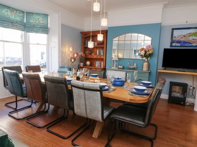 A dining room with a long wooden table set for a meal and multicolored chairs at Seaside House in Weymouth