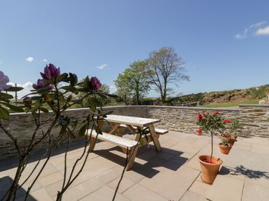 An outdoor patio with wooden picnic tables and potted plants on stone tiles at The Hayloft in Helland near Bodmin
