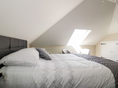 A bedroom with a bed a window two chairs and a sloped ceiling at The Hayloft in Helland near Bodmin