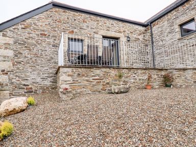 An outdoor stone patio area with a stone wall and a small balcony with chairs and a table at The Hayloft in Helland near Bodmin