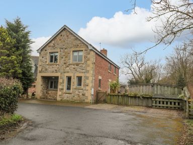 A stone and brick house with a driveway and wooden fence at Ridley Lodge in West Thirston felton