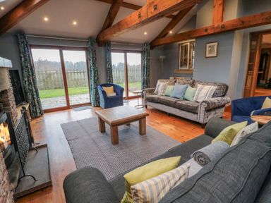 A living room with wooden beams a fireplace two sofas two armchairs a coffee table and large glass doors at Ridley Lodge in West Thirston felton